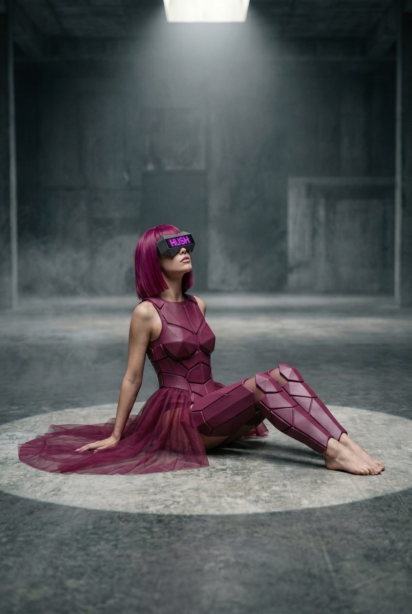 Sestinna seated on the concrete floor, barefoot, looking up into the light